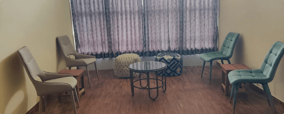 Assorted old metal patio furniture including chairs and a round table in an enclosed space with wood paneled walls and a pink tile floor.